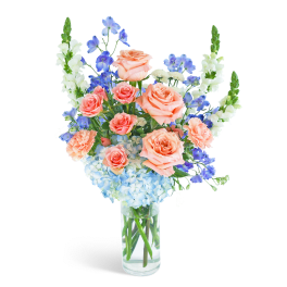 Peach roses and blue flowers in a clear glass vase