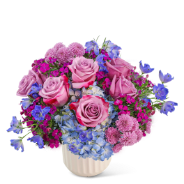 Pink roses and blue flowers arranged in a white vase