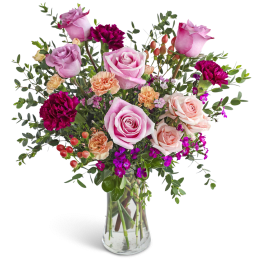 Tall glass vase of pink roses, peach carnations, and dark magenta blooms with berries.