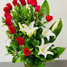 Red roses and white lilies in a tall green vase with a red heart pick