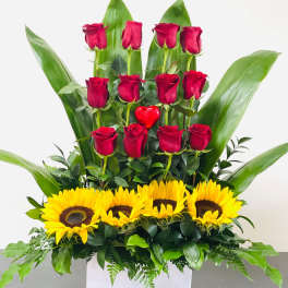 Red roses and sunflowers arranged in a white box with large green leaves