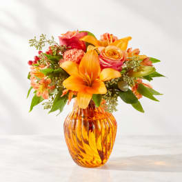 Orange and pink mixed bouquet in an amber glass vase