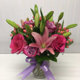Pink lilies and roses with lavender roses in a glass vase tied with a lavender ribbon