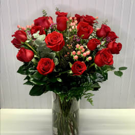 Tall arrangement of red roses with pink berries and filler flowers in a clear glass vase