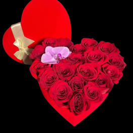Heart-shaped red box filled with red roses and a pink orchid, with a gold-ribboned lid beside it.