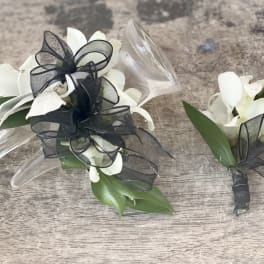 White orchid corsages with black ribbon bows on a wood surface
