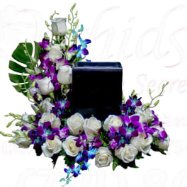 White roses and purple orchids arranged around a black rectangular vase