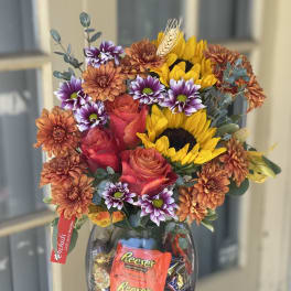 Mixed bouquet of roses, sunflowers, and chrysanthemums in a glass vase with candy