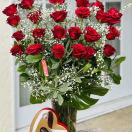 Bouquet of red roses in a glass vase with baby's breath and a heart-shaped chocolate box