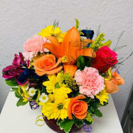 Colorful bouquet with roses, lilies, daisies, and carnations in a low vase