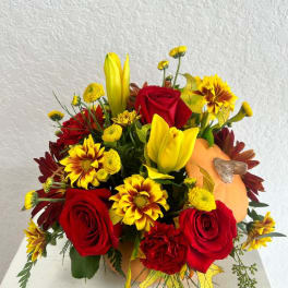 Bouquet of red roses, yellow lilies, and daisies with a small pumpkin