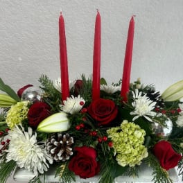 Red candles in a floral centerpiece with roses, lilies, and white blooms