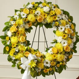 Yellow and white floral wreath on a black stand with a white ribbon