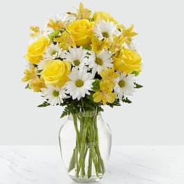 Yellow roses and white daisies in a clear glass vase
