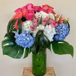 Bouquet of pink roses, tulips, white flowers, and blue hydrangeas in a green vase