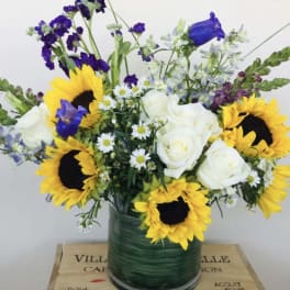 Bouquet of sunflowers, white roses, and purple flowers in a glass vase