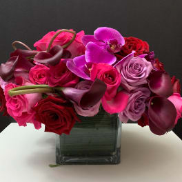 Bouquet of pink and red roses with purple orchids in a square glass vase