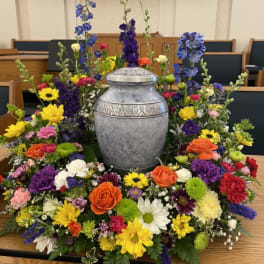 Colorful funeral urn surround with mixed flowers around a silver urn