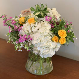 White hydrangeas with yellow roses and pink flowers in a glass vase