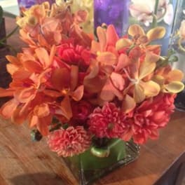 Orange and pink floral arrangement in a square glass vase