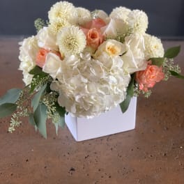 White and peach floral arrangement in a white square vase