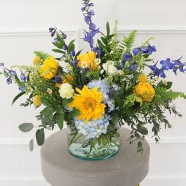 Mixed bouquet in a clear glass vase with yellow, blue, and white flowers