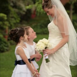 Bride in a white dress holding a white bouquet beside two flower girls
