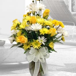 Yellow and white flowers in a glass vase with a ribbon bow