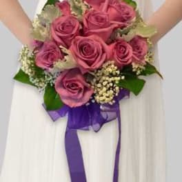 Pink rose bouquet with a purple ribbon held in front of a white dress