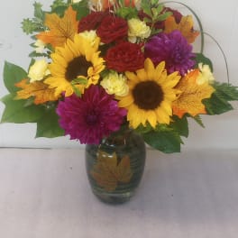 Bouquet of sunflowers, red roses, and purple mums in a glass vase