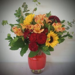 Mixed bouquet of red roses, sunflowers, and peach alstroemeria in a glass vase