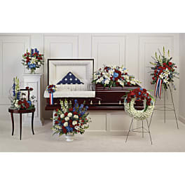 Funeral casket surrounded by red, white, and blue floral sprays