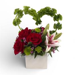 Red roses and white lilies in a white square vase with a green heart handle