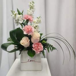 Pink roses and carnations with white blooms in a square vase