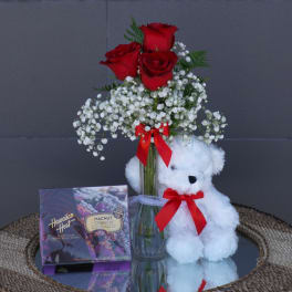 Red roses in a glass vase with a teddy bear and chocolate box