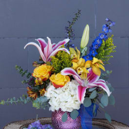 Mixed bouquet with lilies, roses, hydrangea, and blue delphinium in a pink vase