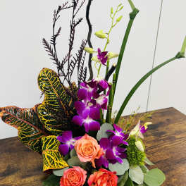 Tropical floral arrangement with purple orchids and coral roses