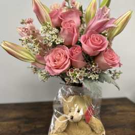 Pink roses and lilies in a wrapped bouquet with a teddy bear