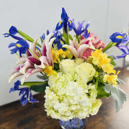 Bouquet of blue irises, white lilies, and pale hydrangeas in a glass vase