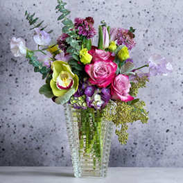 Mixed bouquet of pink roses, orchids, and calla lilies in a clear vase