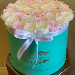 Pink and white roses arranged in a turquoise round box with a ribbon