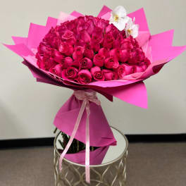 Large bouquet of hot pink roses with white orchids wrapped in bright pink paper