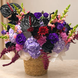 Purple and pink floral arrangement in a woven basket with black anthuriums