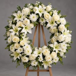 White floral wreath on a wooden easel with lilies, roses, and mums