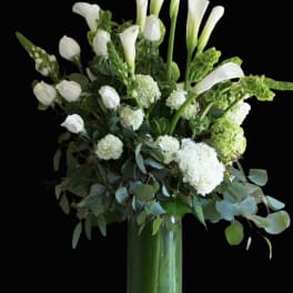 White calla lilies and hydrangeas in a tall glass vase