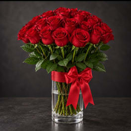 Red roses arranged in a clear glass vase with a red ribbon bow