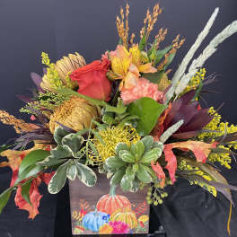 Autumn floral arrangement in a painted pumpkin box with red, yellow, and peach blooms