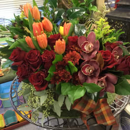 Bouquet of red roses, orange tulips, and orchids in a decorative container