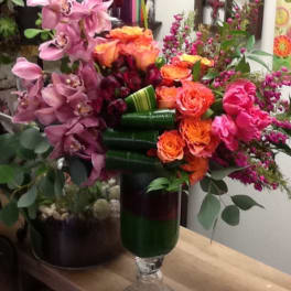 Mixed bouquet with pink orchids, orange roses, and magenta flowers in a glass vase