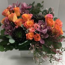 Bouquet of orange roses and purple orchids in a white container